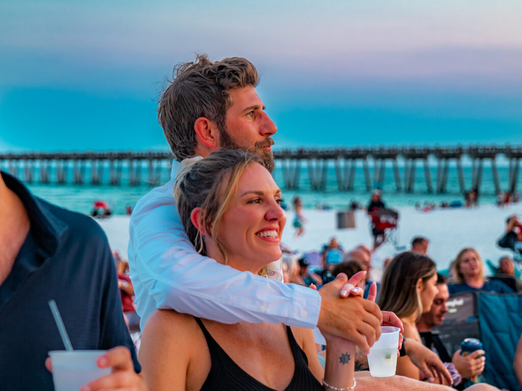 A couple embracing while at Bands on the Beach, the Pensacola Pier behind them. 