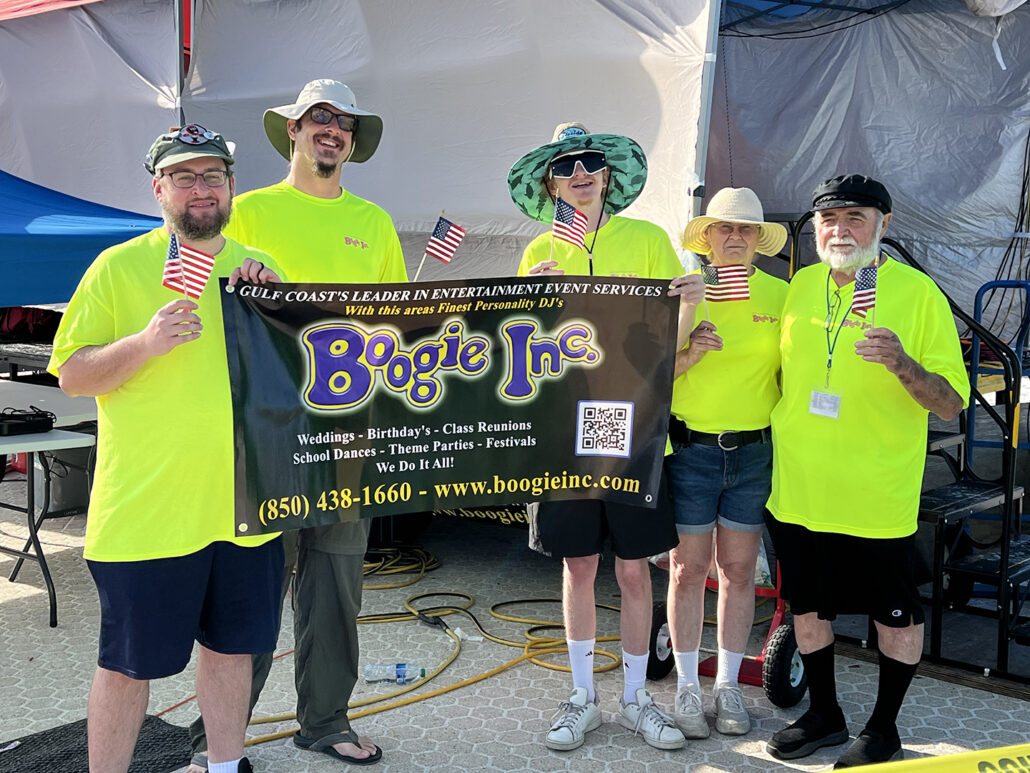 Five men in bright yellow shirts holding a Boogie Inc. banner and small American Flags.