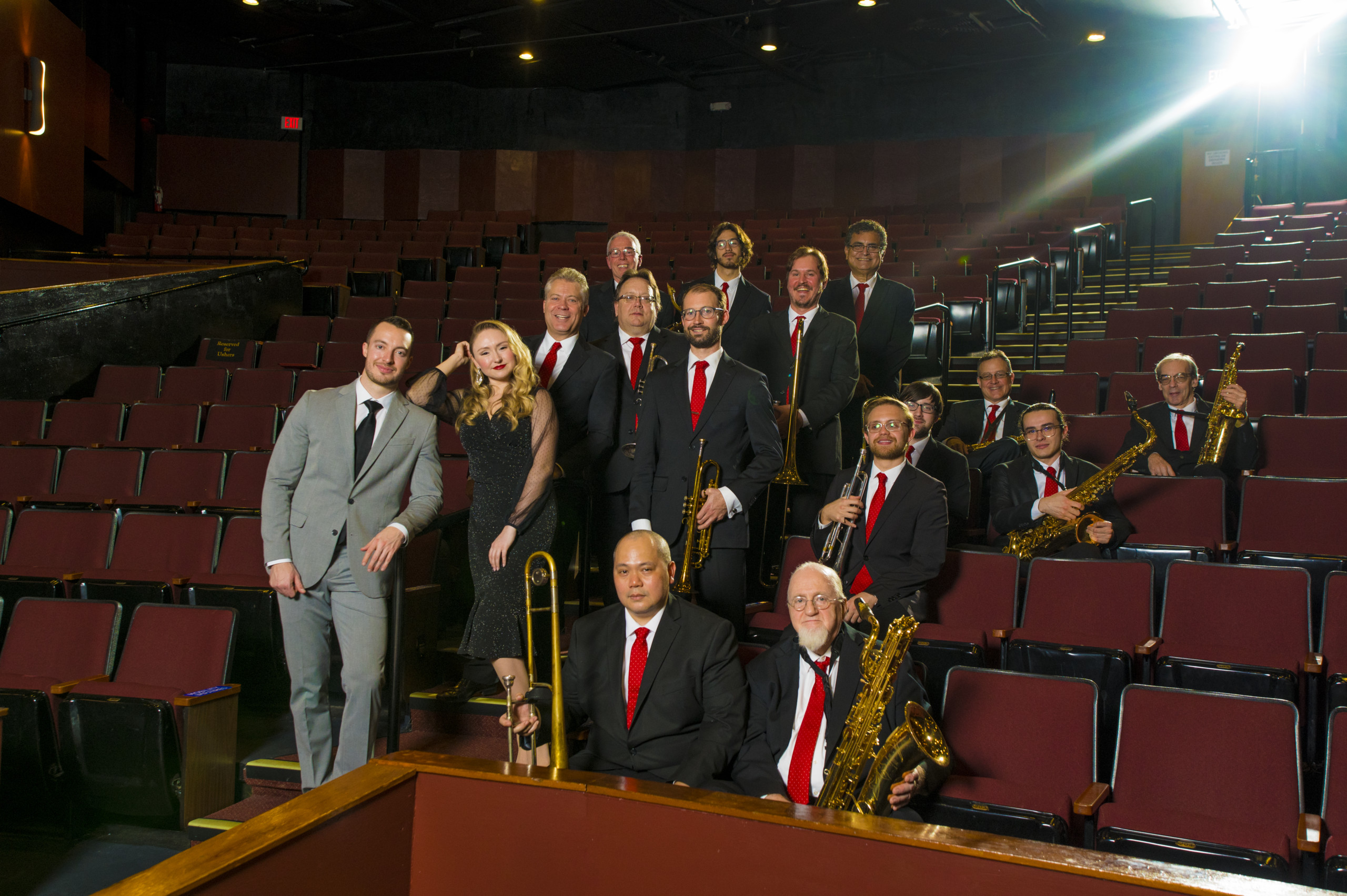 Members of the Glenn Miller Orchestra stanid together with their instrument in a theater.