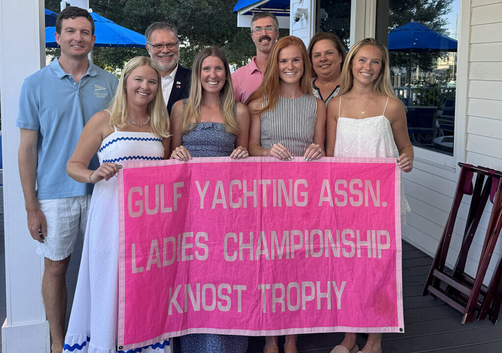 Group of people holding up a pink banner in celebration of the Yacht Club Women Winning the Knost Championship