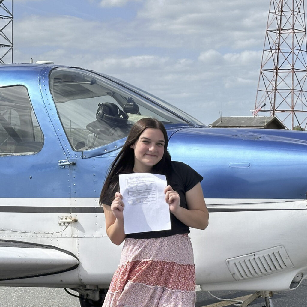 Emily Shelton stands in front of a plane holding a piece of paper. 