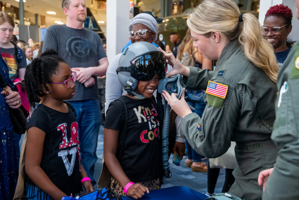 A woman helps put a helmet on a girl while another girl watches at the National Naval Aviation Museum's Girls in Aviation Day. 