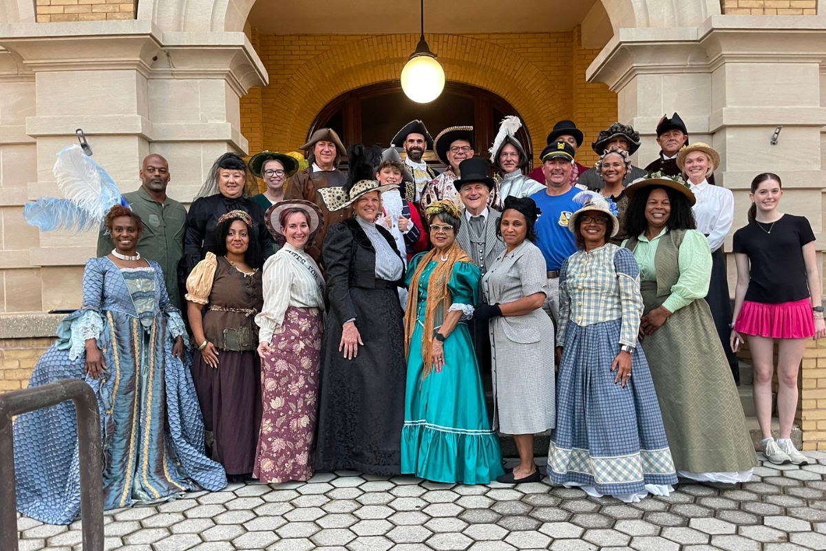 A group of people dressed in historic clothing stand in front of the Pensacola Museum of History